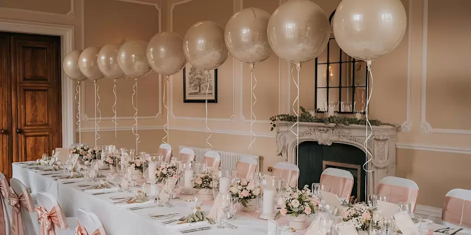 A wedding dining table set up with baby pink balloons and floral arrangements.